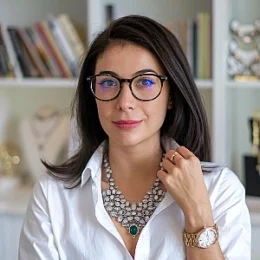 Woman with glasses and a necklace, wearing a white shirt, looking at the camera